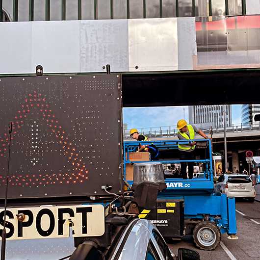 Wiener Linien Branding Steg Erdberg: Arbeiter auf Hebebühne montieren Plakat. Verkehrsschild im Vordergrund.