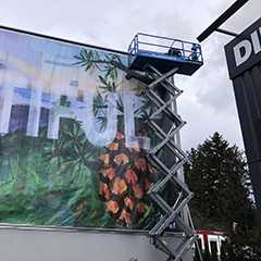 Montage von Werbebannern mit Rahmensystemen. Scherenbühne vor großem Wandbild.