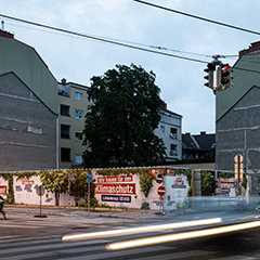 Baustellenverplankung in Wien. Bauzaun mit Klimaschutz-Werbung an einer Wiener Kreuzung. Rotes Ampellicht.
