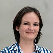 Yvonne Munda Porträt. Frau mit braunen Haaren und gestreiftem Hemd lächelt.