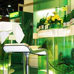 Messestand: Grüner Messestand mit Barhocker, Getränken und Blumen. Messe-Impression.