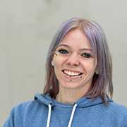 Christine Tepper: Porträt einer lächelnden Frau mit Piercings und lila Haaren.