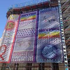 Fassade mit Bannering. Kunstinstallation mit bunten Motiven am Baugerüst. Fassadenkunst in der Stadt.