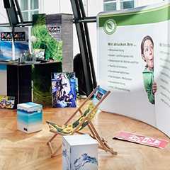 Präsentationssysteme Messe: Messestand mit Werbedisplays, Liegestuhl und bedruckten Würfeln.