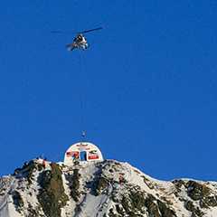 Helikopter Montage: Messe auf schneebedecktem Berggipfel. Zelt wird per Helikopter montiert.