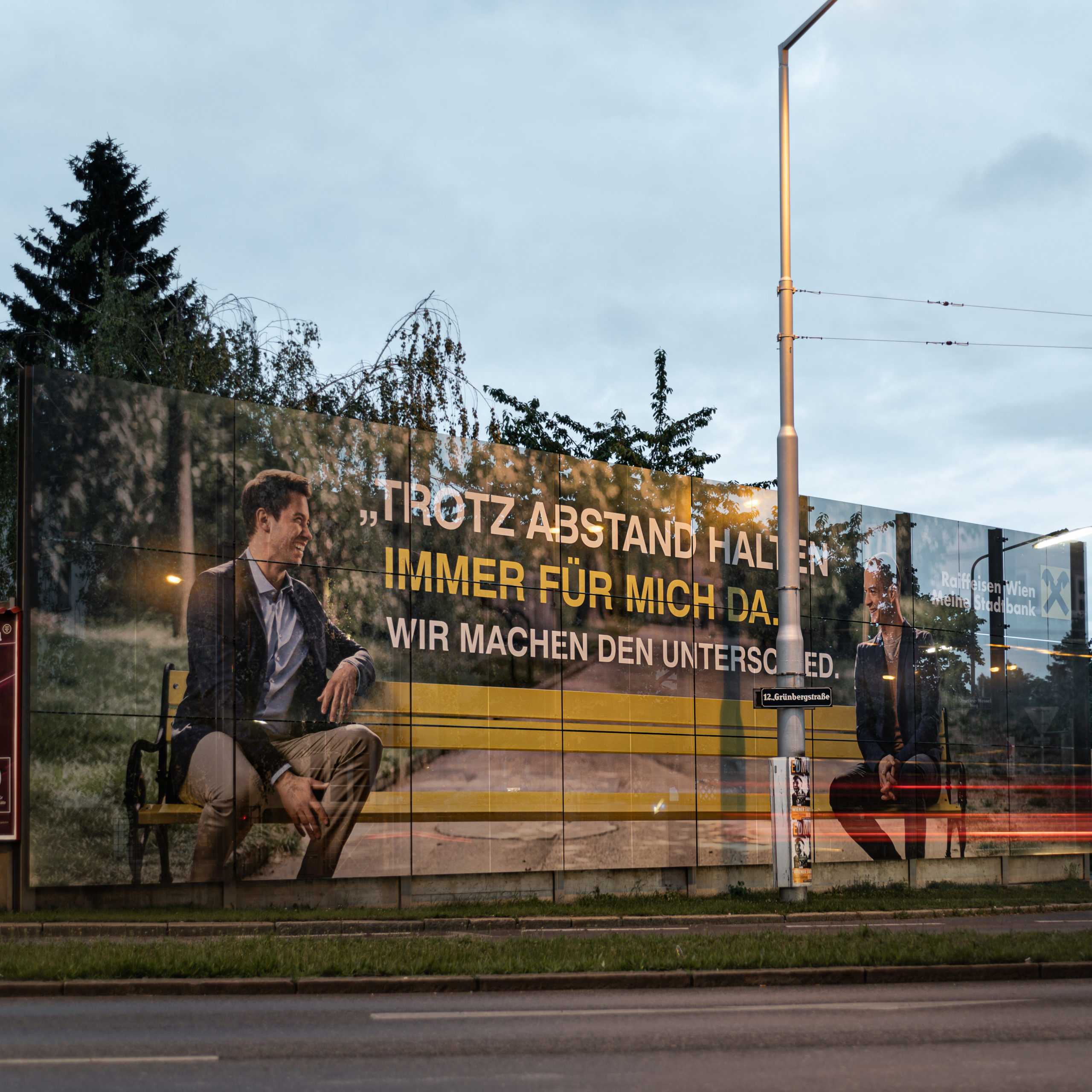 Aussenwerbung Teaserbild: Raiffeisen Bank Kampagne Trotz Abstand für mich da. Plakat mit Personen auf Bank.