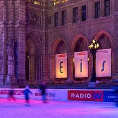 Eistraum Wien Rathausplatz: Eisfläche mit Bannern vor dem Wiener Rathaus bei Nacht.