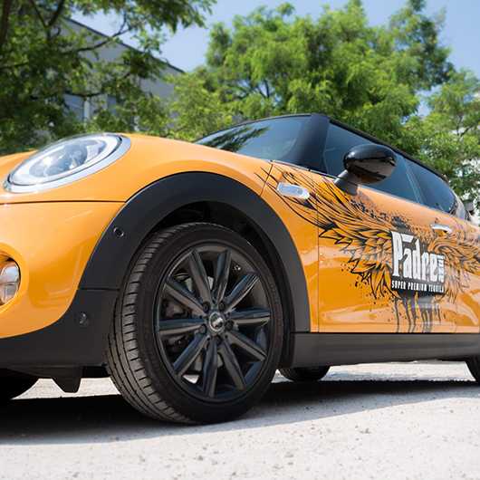 Gelber Mini Cooper mit Padre Tequila Werbung. Fahrzeug vor Gebäude und Bäumen.