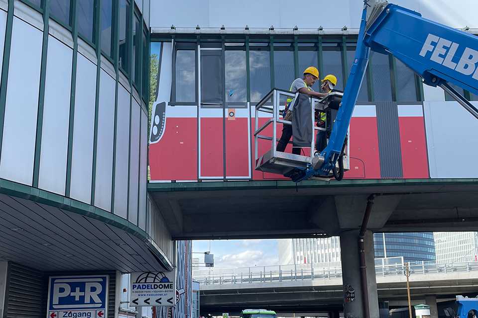 Branding Steg Erdberg: Wiener Linien Werbung wird montiert. Arbeiter auf Hebebühne.