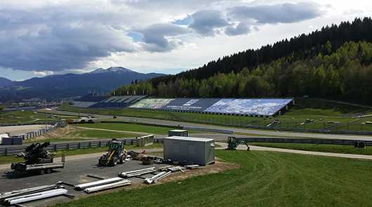 Outdoor Events: Rennstrecke mit Tribüne und Baumaschinen vor Bergkulisse.
