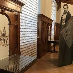Ausstellungen: Museumsansicht mit Textwand, Holzvertäfelung und Portrait.